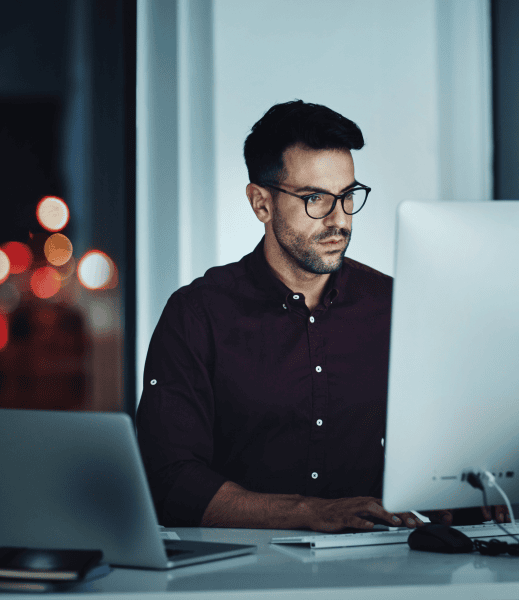Man working on a laptop and a separate screen in the office at night.