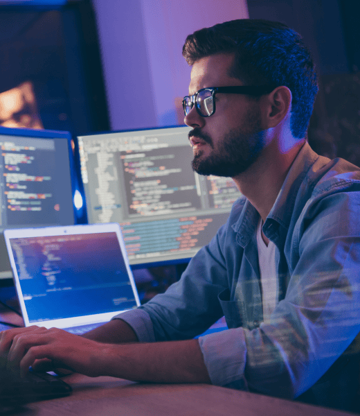 A man sitting in a dark office. There are multiple screens in the background.