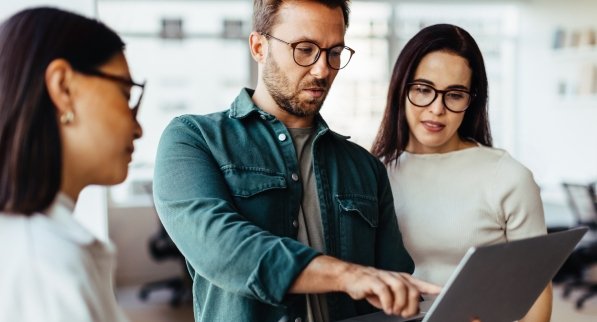 Three coworkers in an office. Two of them are looking at a screen.